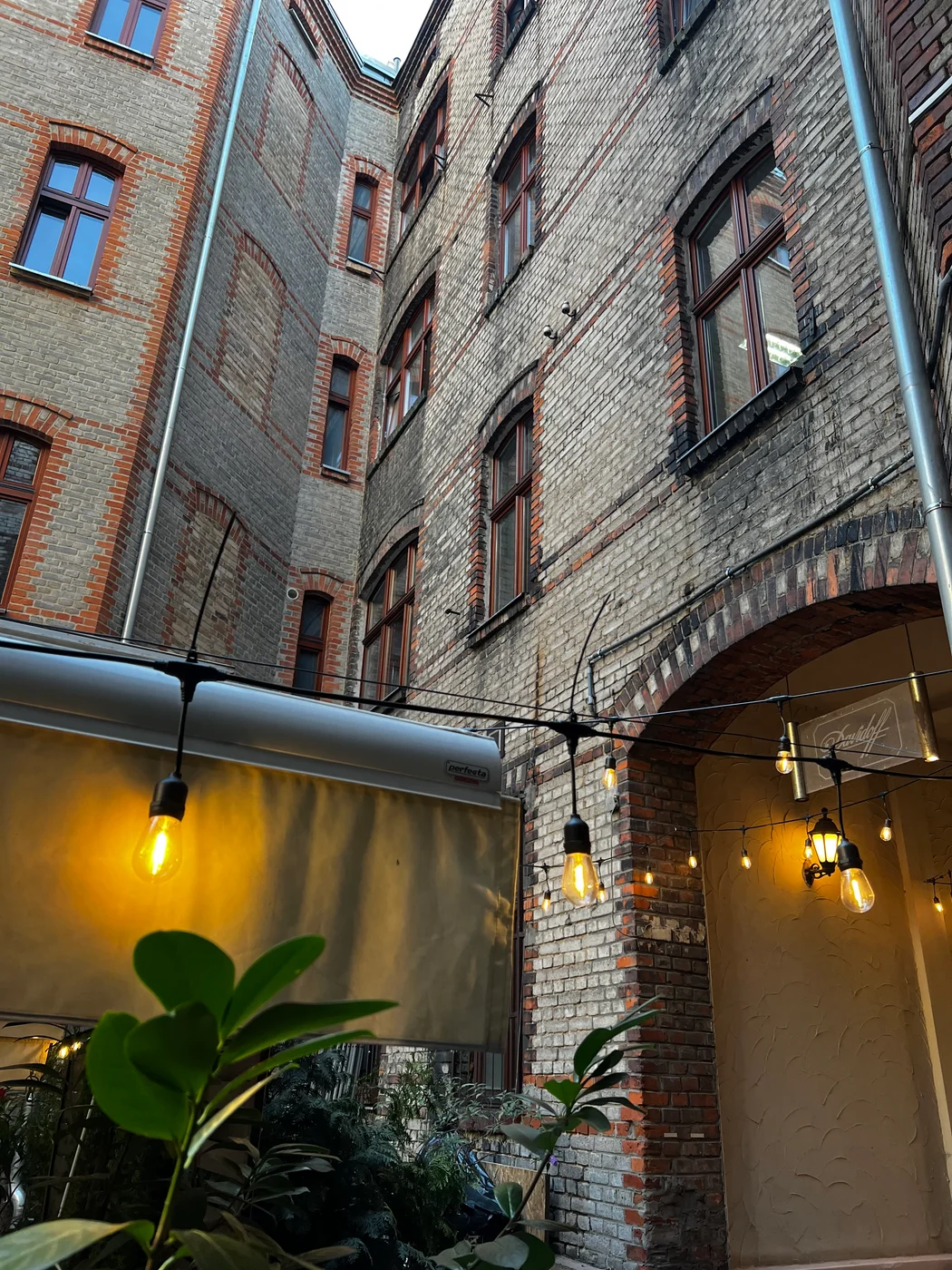 Ceglane elewacje kamienic, zielone rośliny i girlanda ciepłych świateł na dziedzińcu Sorrento